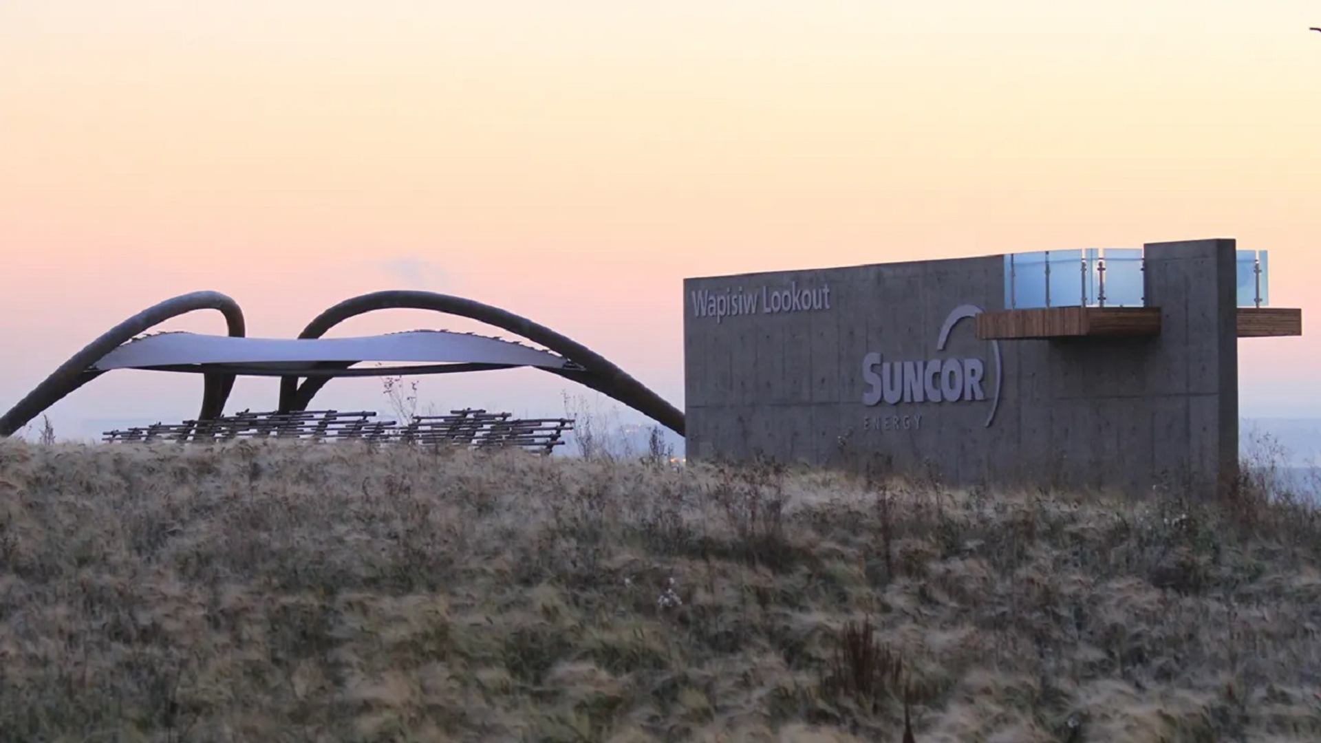 Concrete Wapisiw Lookout structure with Suncor Energy sign beside curved canopy and grass.