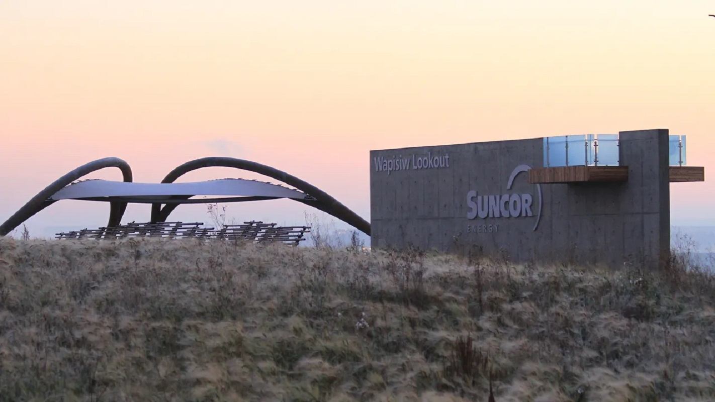 Concrete Wapisiw Lookout structure with Suncor Energy sign beside curved canopy and grass.