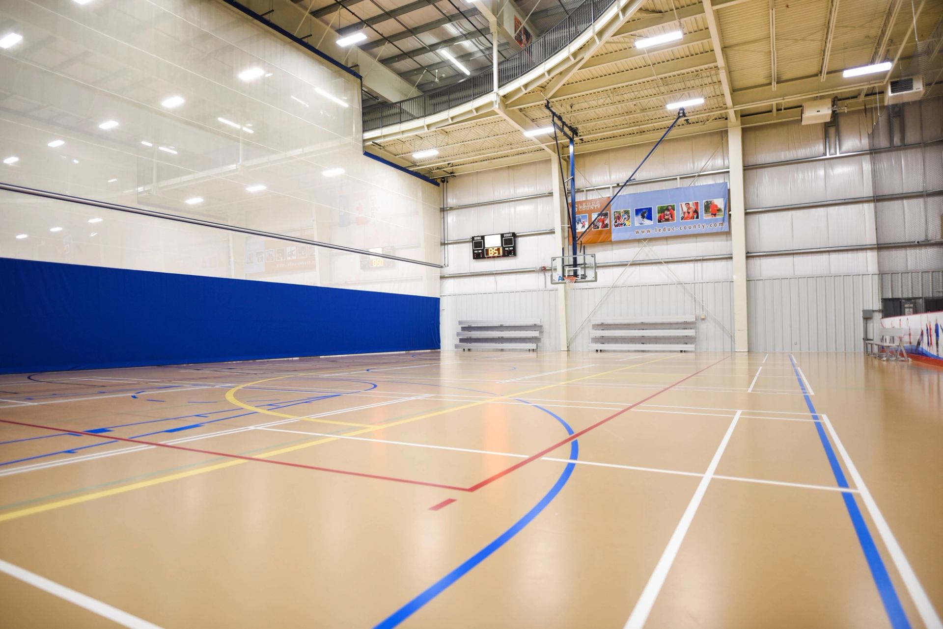 Indoor basketball court with polished floor, hoop, and blue wall padding.