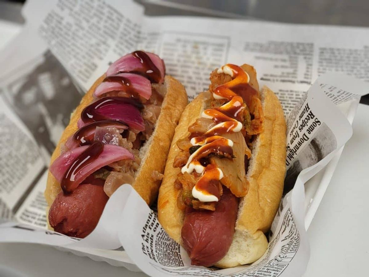 Two gourmet hot dogs with pickled onions and special toppings