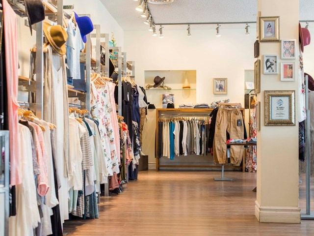 Clothing racks and framed artwork inside a retail shop with a central wardrobe display.