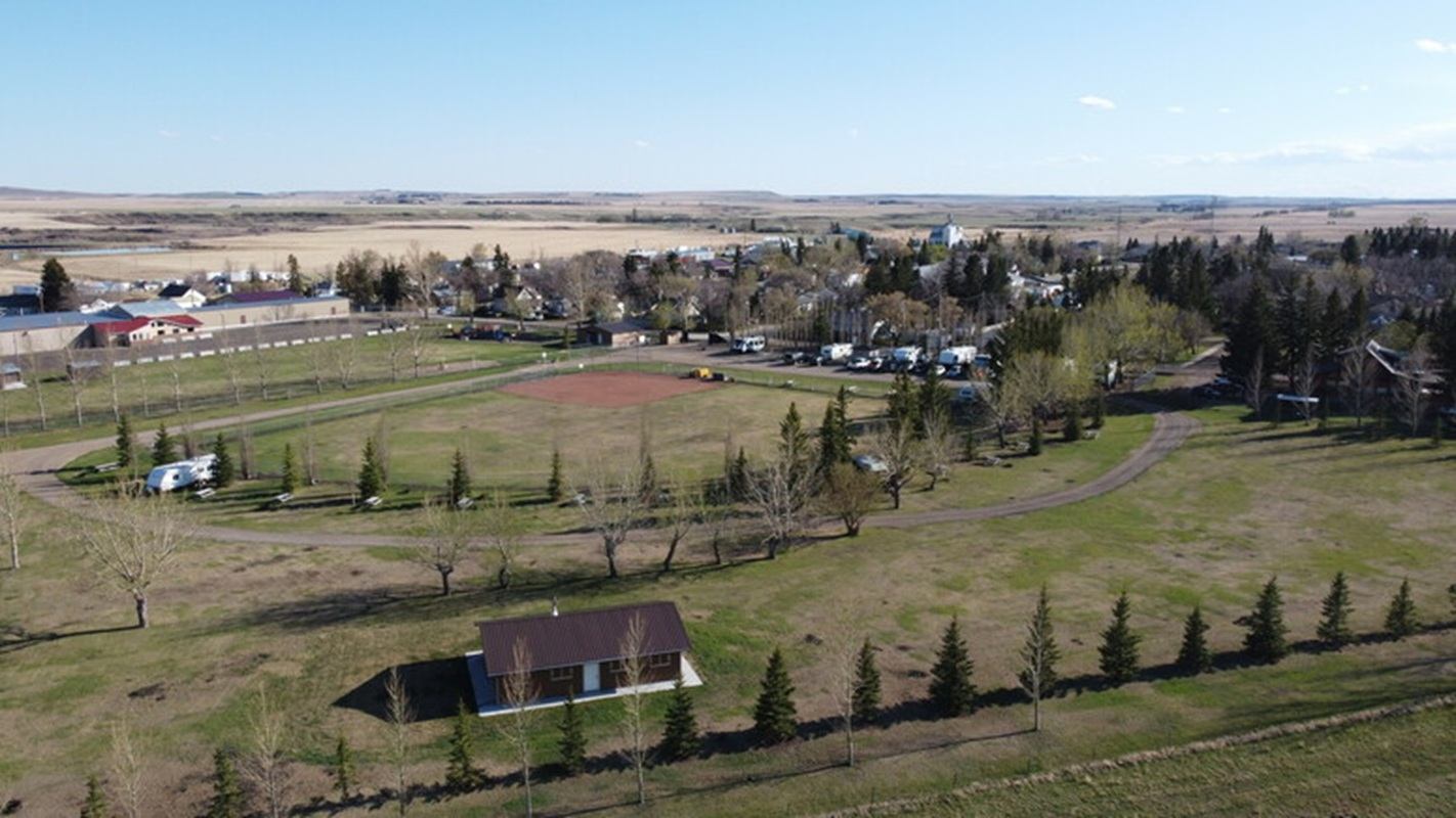 Aerial view of a rural park, baseball diamond, buildings, trees and surrounding farmland.