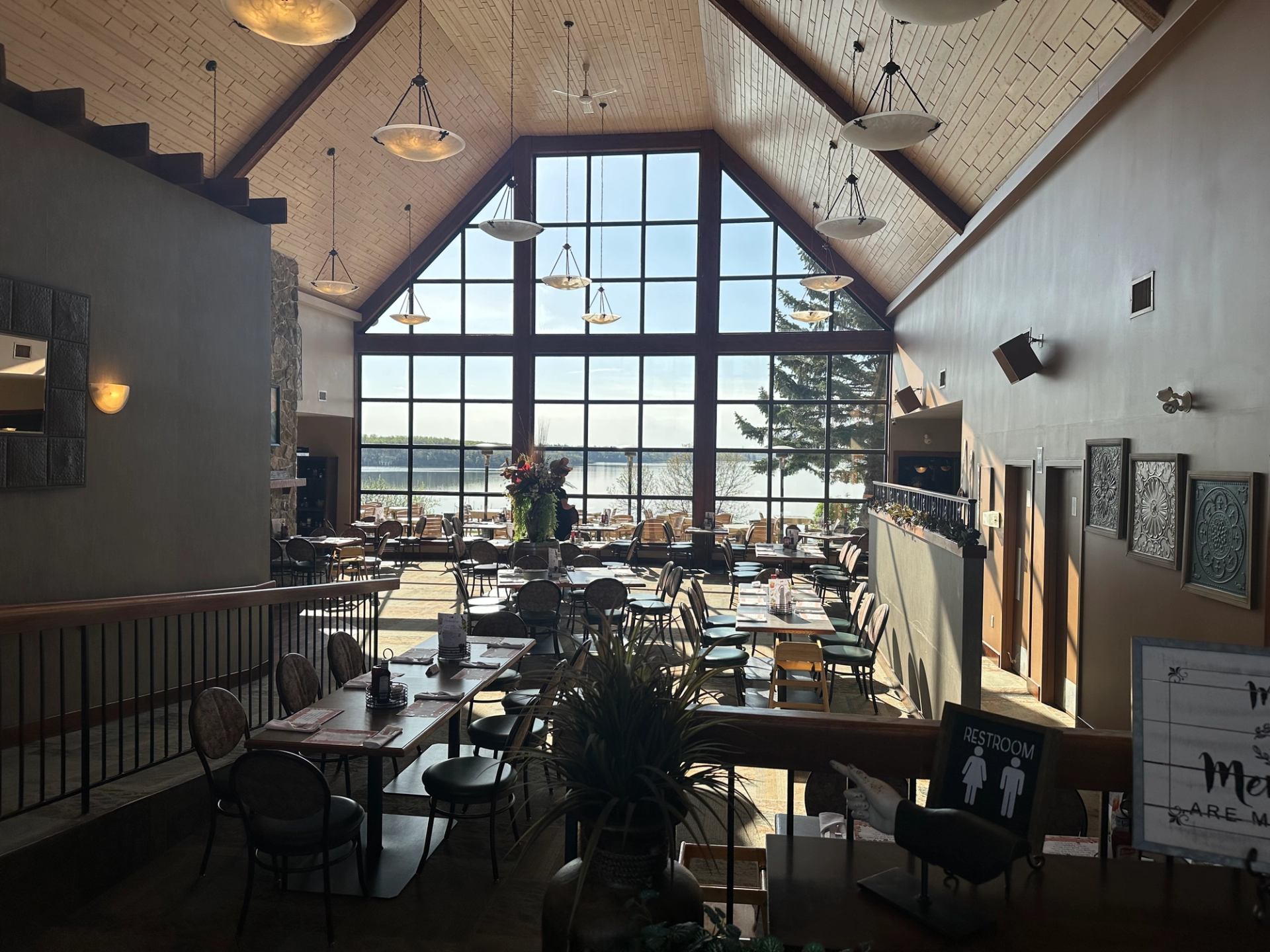 Spacious restaurant interior with high wooden ceiling and large windows overlooking a lake.