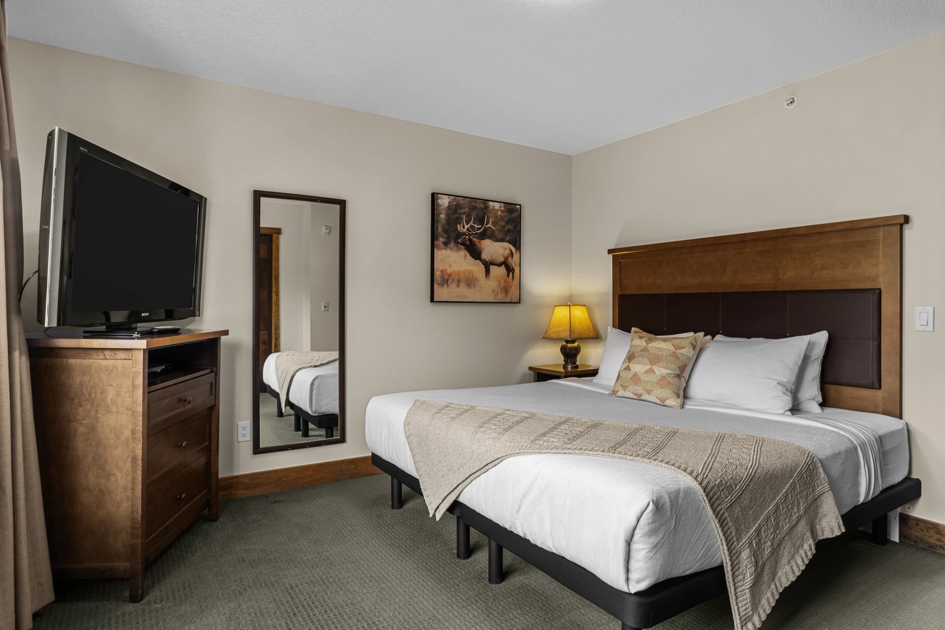 Hotel room with two beds, wooden headboard, television, mirror and elk artwork.