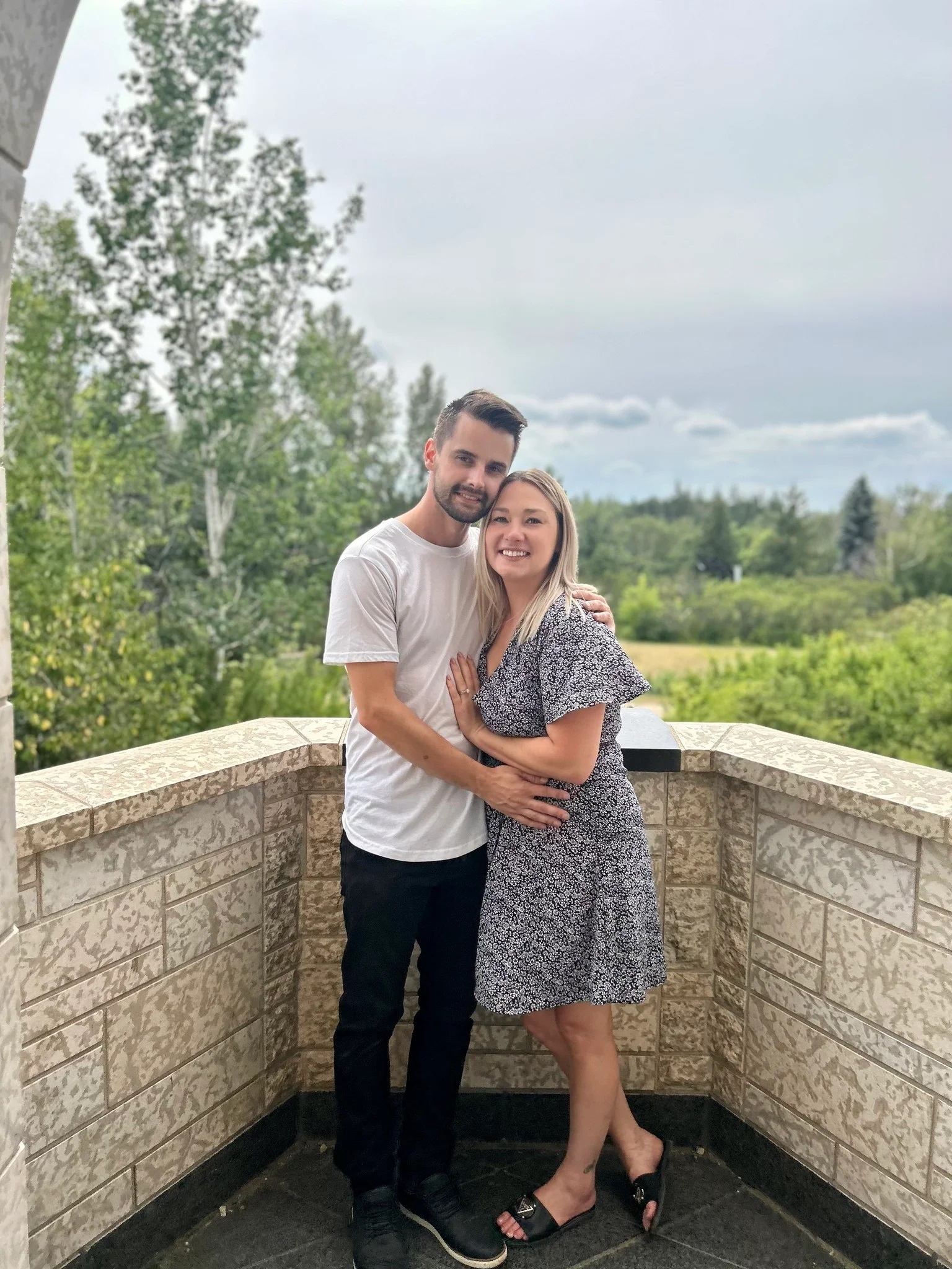 The owners of Battle River Beer Co. stand together on a stone balcony overlooking trees and sky.