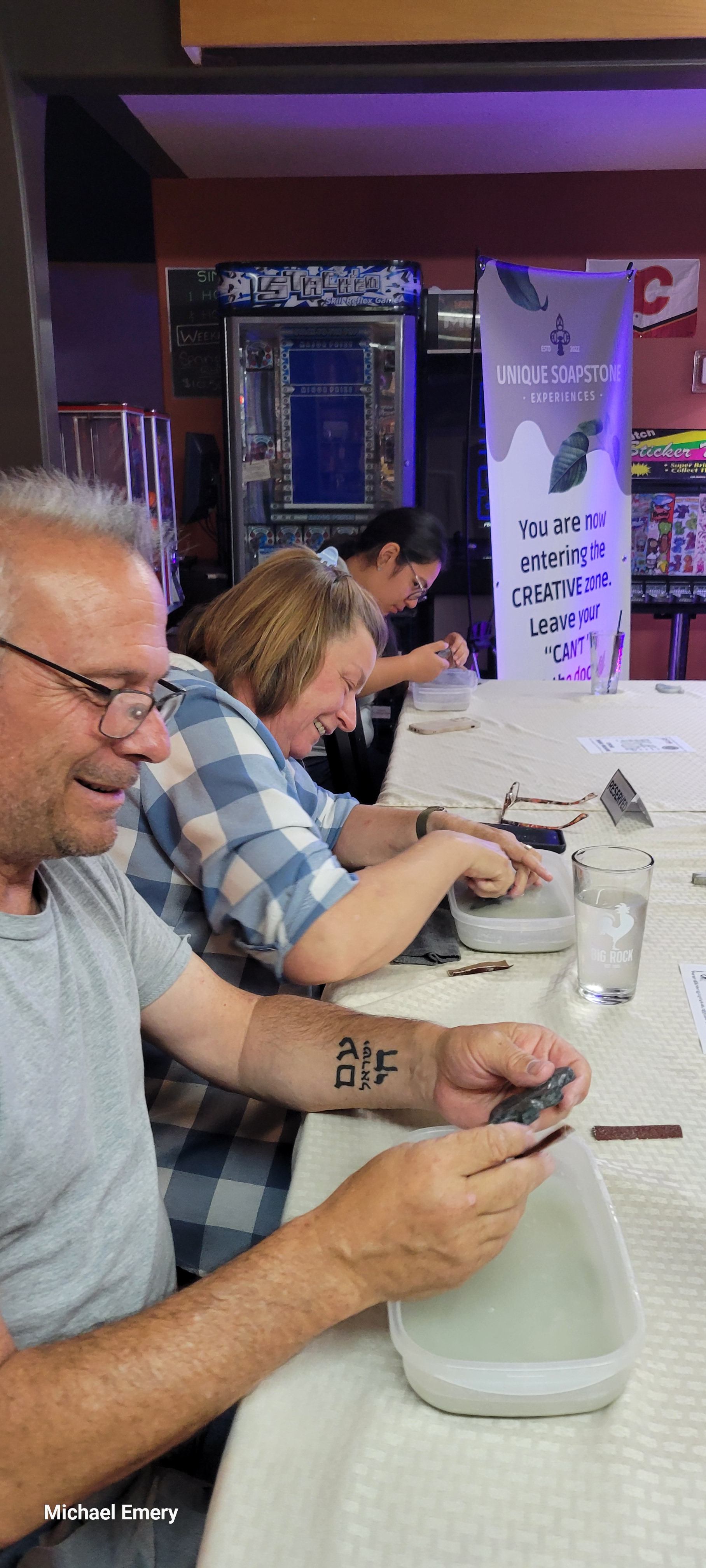 People polish soapstone pieces over water-filled trays at a workshop table.