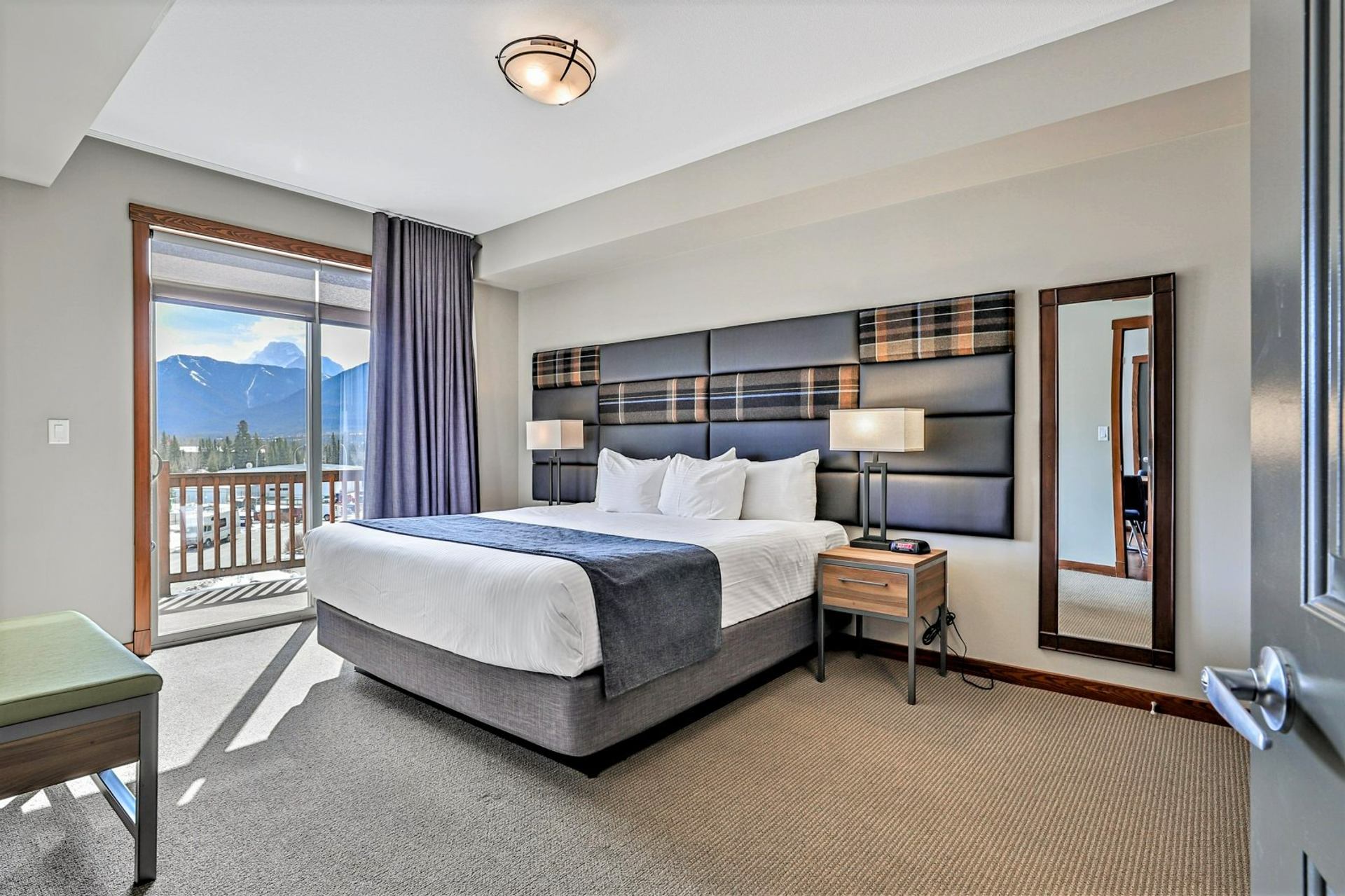 Bedroom with a large bed, bedside lamps, wall mirror and mountain-view balcony.