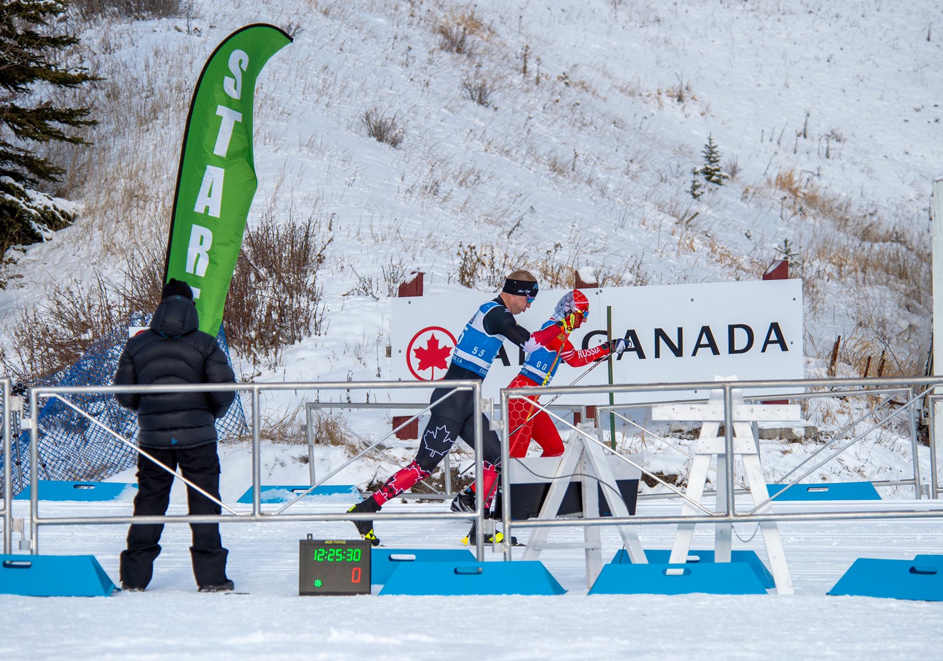 Two para skiers start a race in Canmore as a timer counts down and a Canada sign marks the venue.