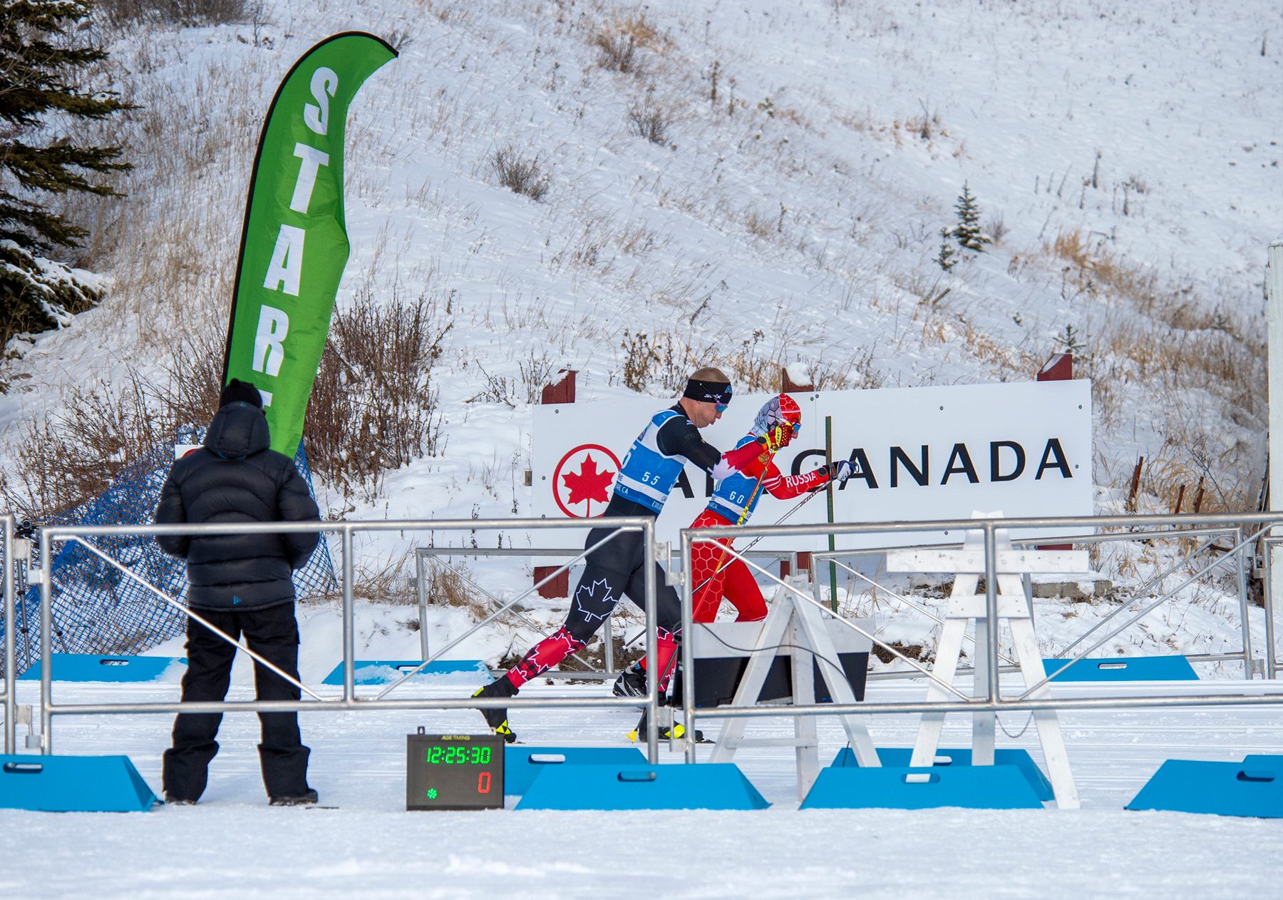 Two para skiers start a race in Canmore as a timer counts down and a Canada sign marks the venue.