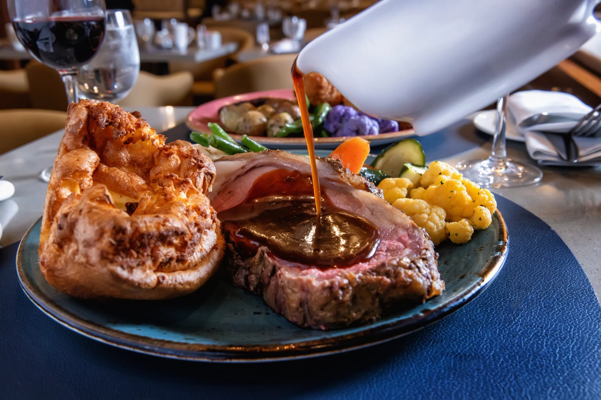 Roast beef with gravy, Yorkshire pudding and mixed vegetables on a restaurant table.