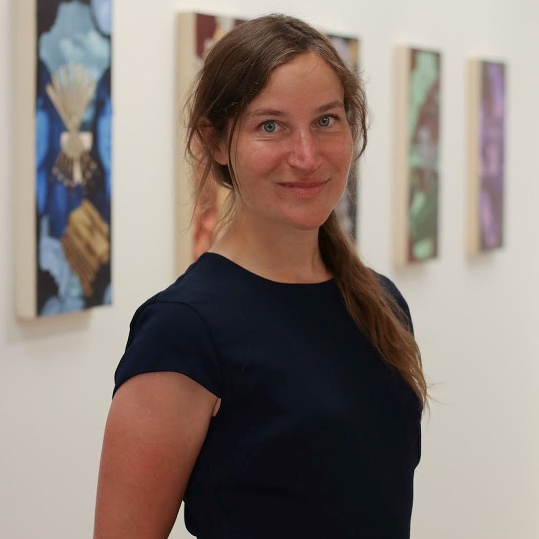 Person in a black shirt standing in front of framed artworks in an art gallery.
