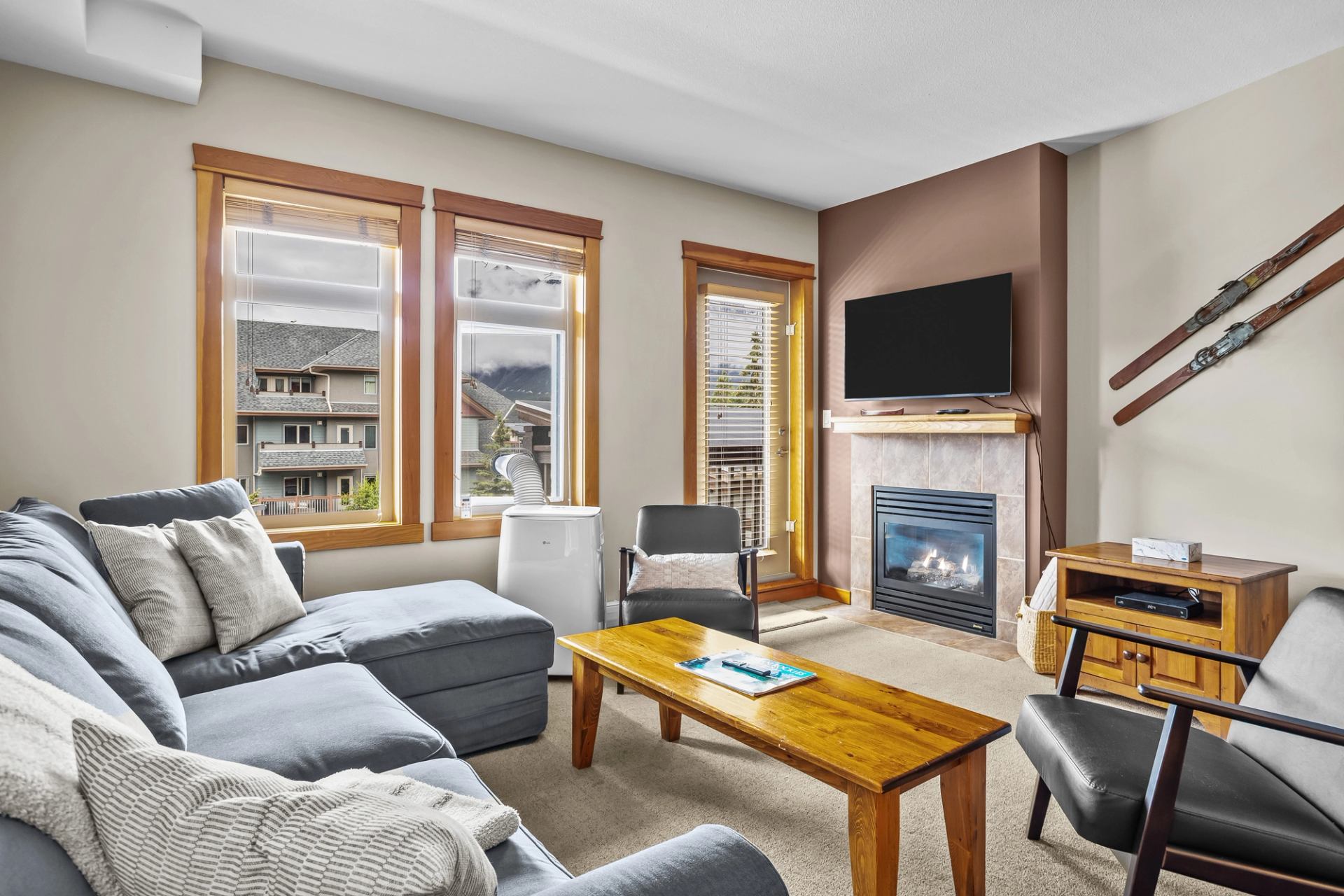 Living room with grey sectional, wooden coffee table, fireplace and wall-mounted television.