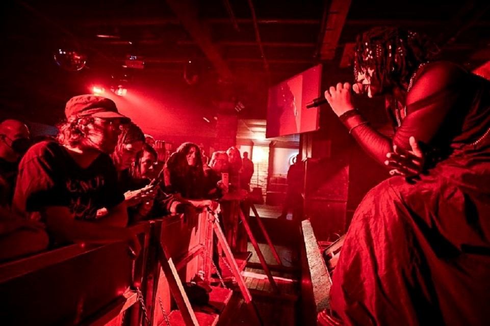 Singer in red stage lighting performs close to audience leaning on metal barrier.