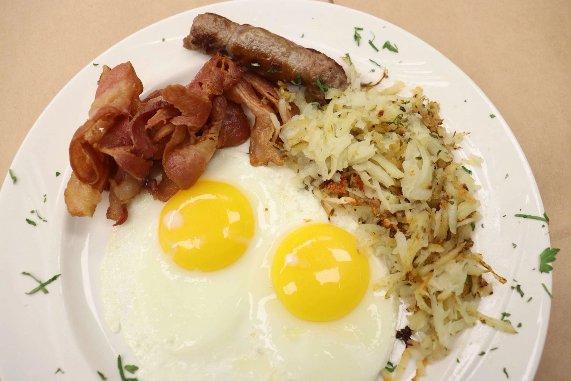 Breakfast plate with sunny-side eggs, crispy bacon, sausage, and golden hash browns.