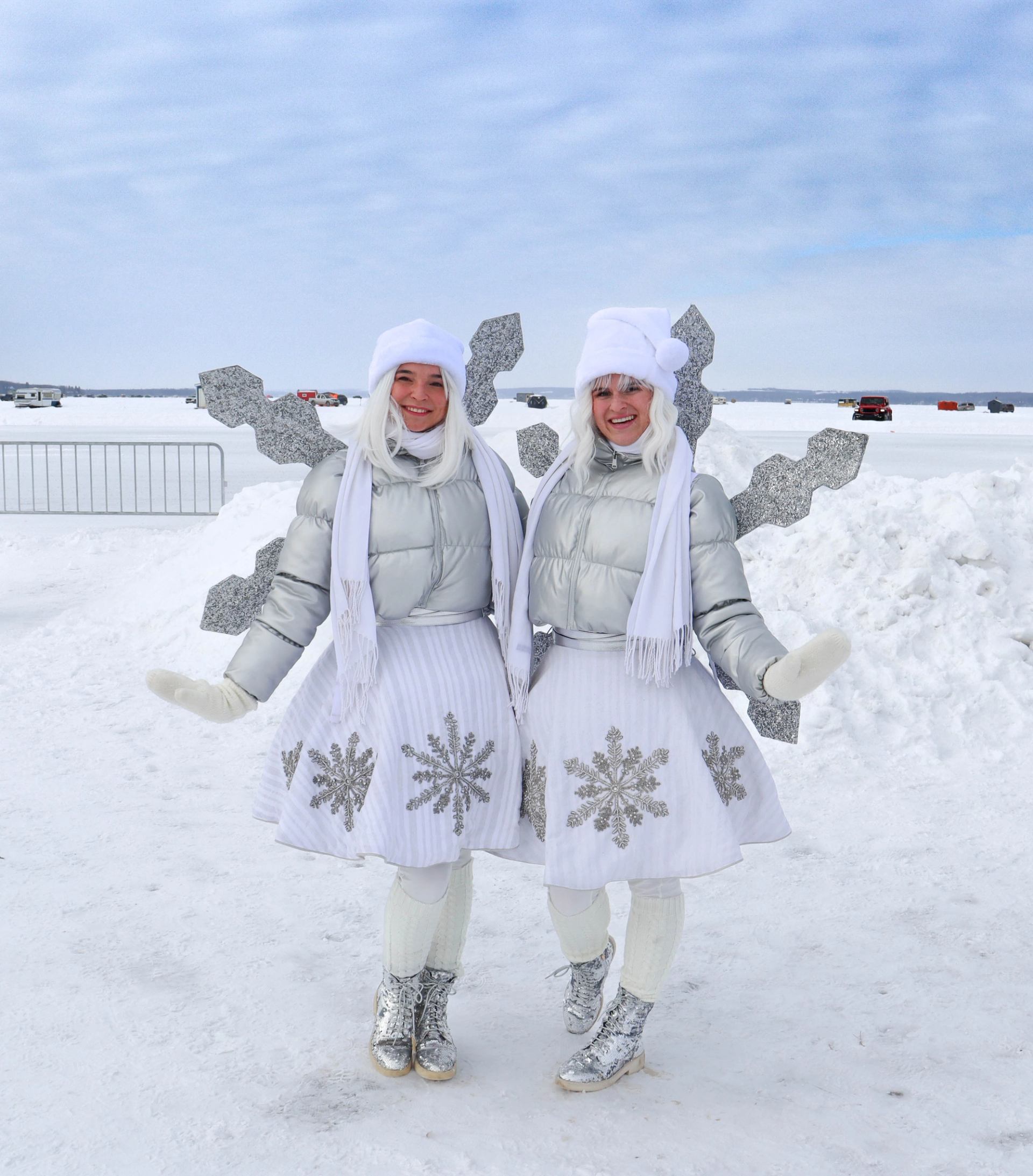 Two people pose in white winter outfits beside a carved ice dragon on frozen lake.