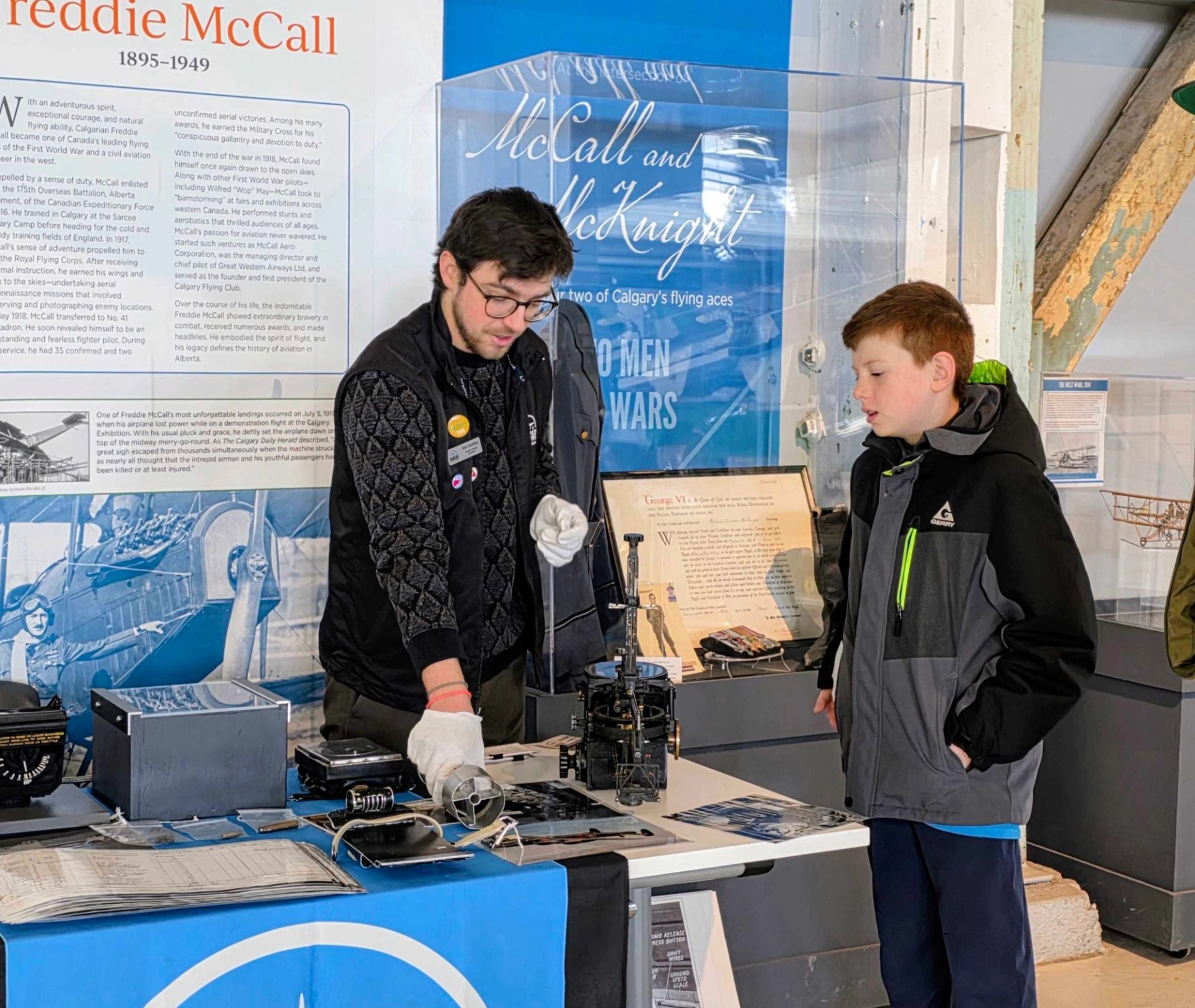 An adult in white gloves explains old mechanical equipment to a young boy at a museum exhibit.