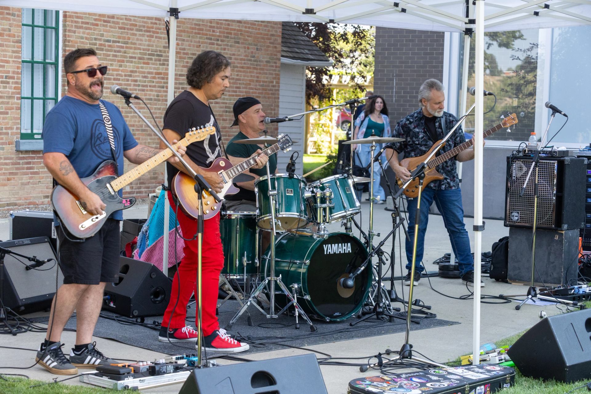 Outdoor rock band performing under a canopy with guitars, drums and amplifiers.