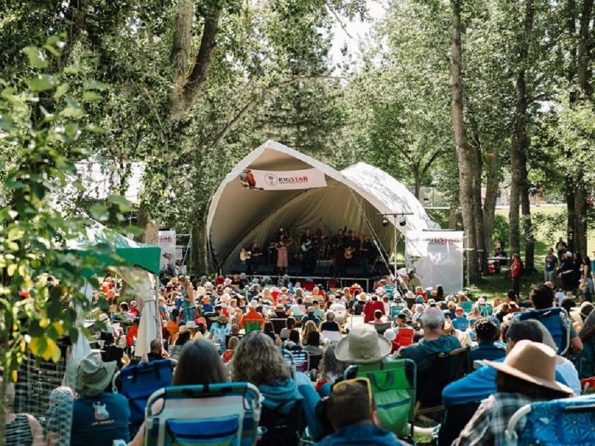 Outdoor music festival crowd sitting on lawn chairs facing a band performing on stage.