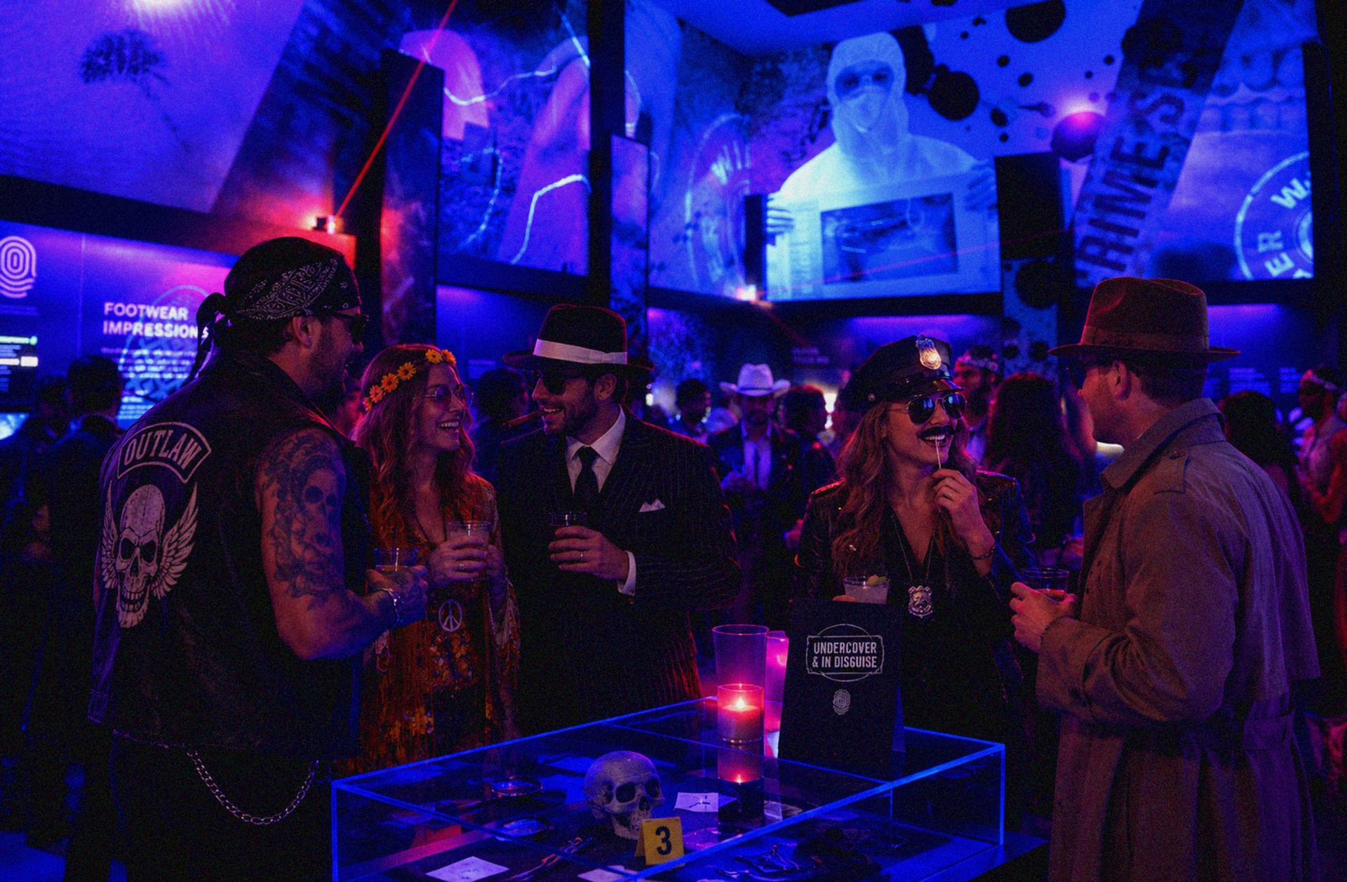 Costumed guests gather around a display table under blue and purple lighting.