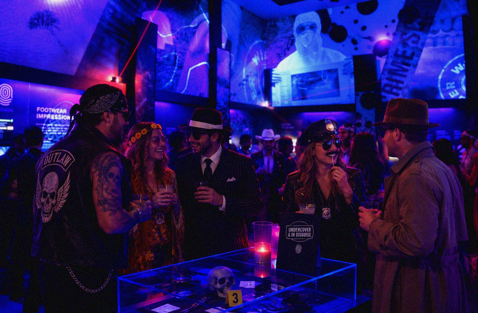 Costumed guests gather around a display table under blue and purple lighting.