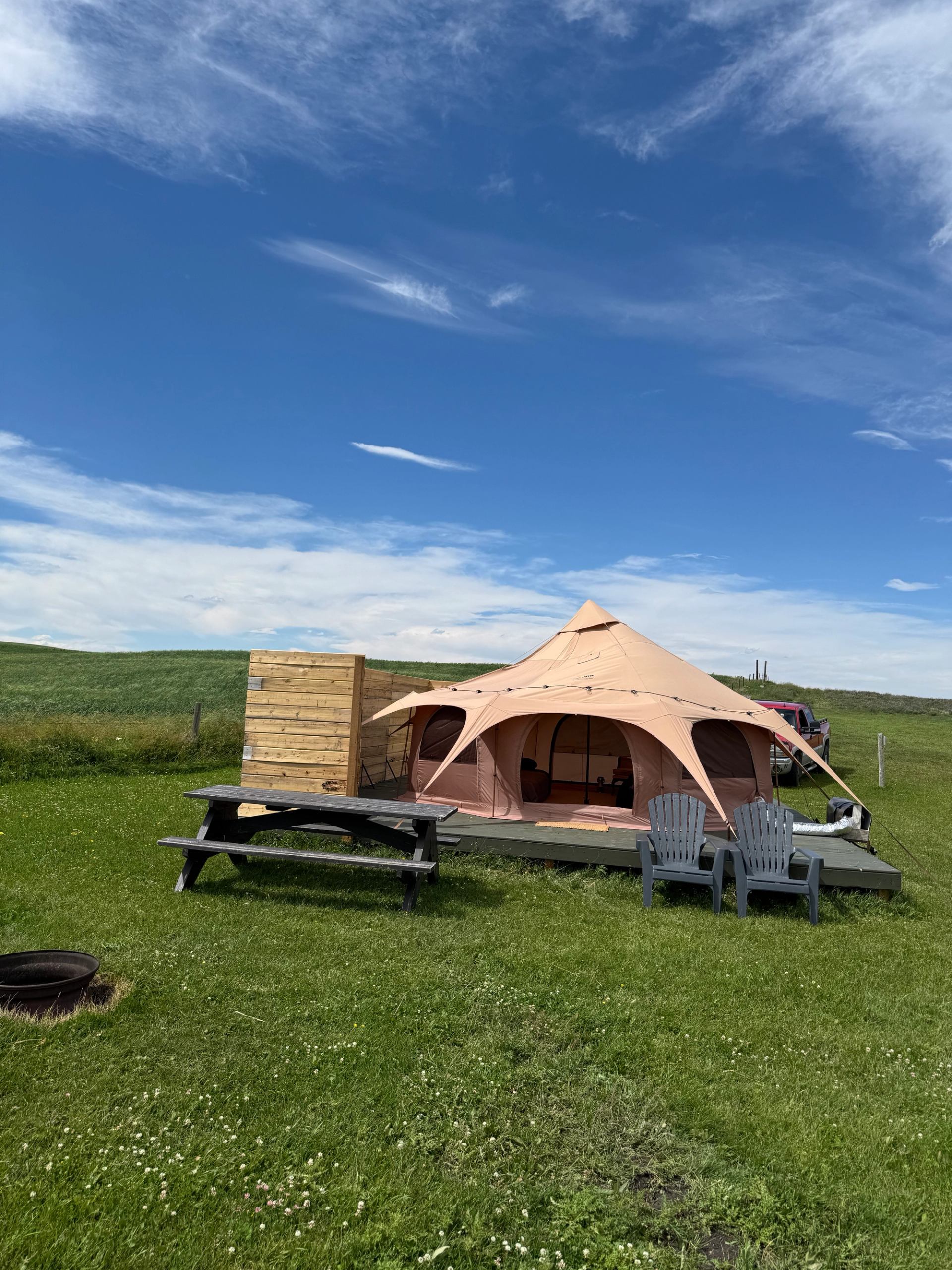 A large canvas glamping tent with seating, set on open green prairie land.
