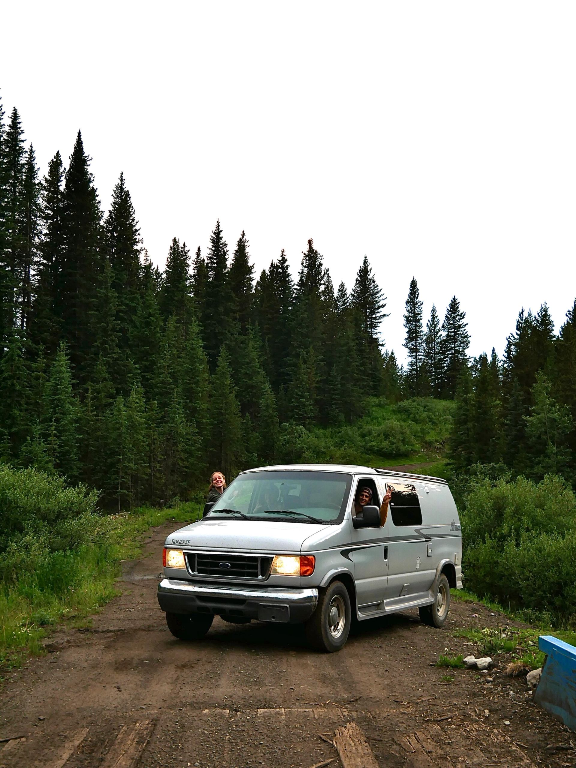 White camper van parked in forest with two people enjoying nature.
