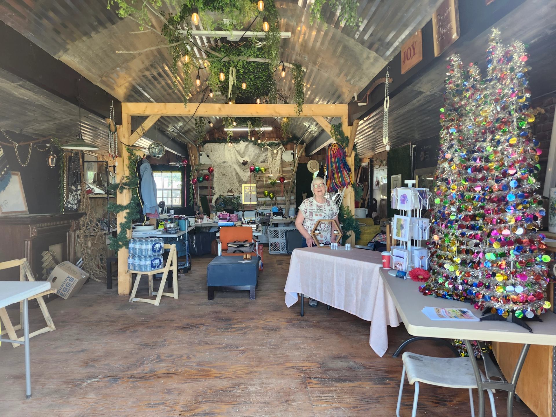 Craft workshop interior with decorated tinsel tree, tables of supplies, and person arranging items.