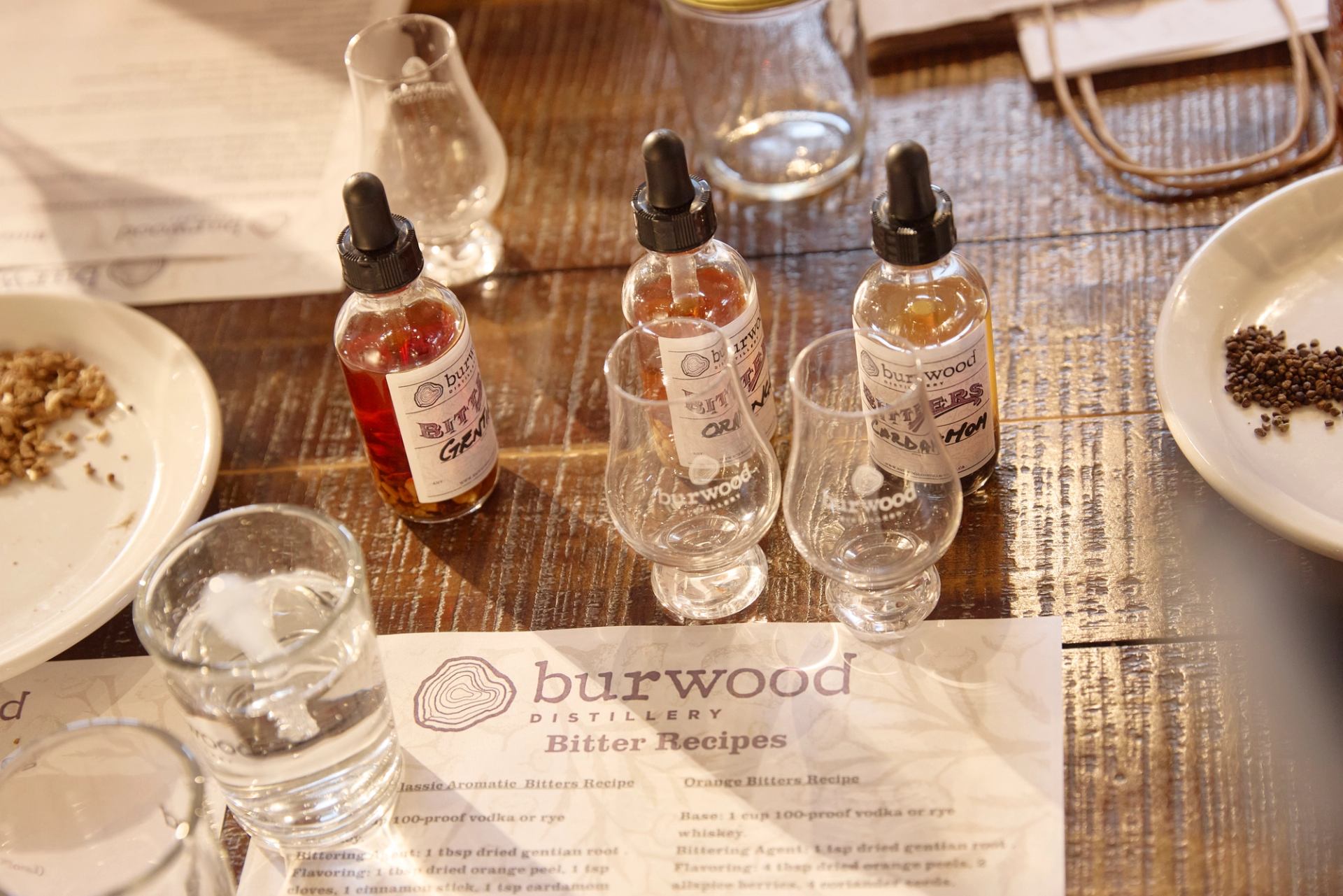 Bitters bottles, tasting glasses, spices and recipe sheet on a wooden table.