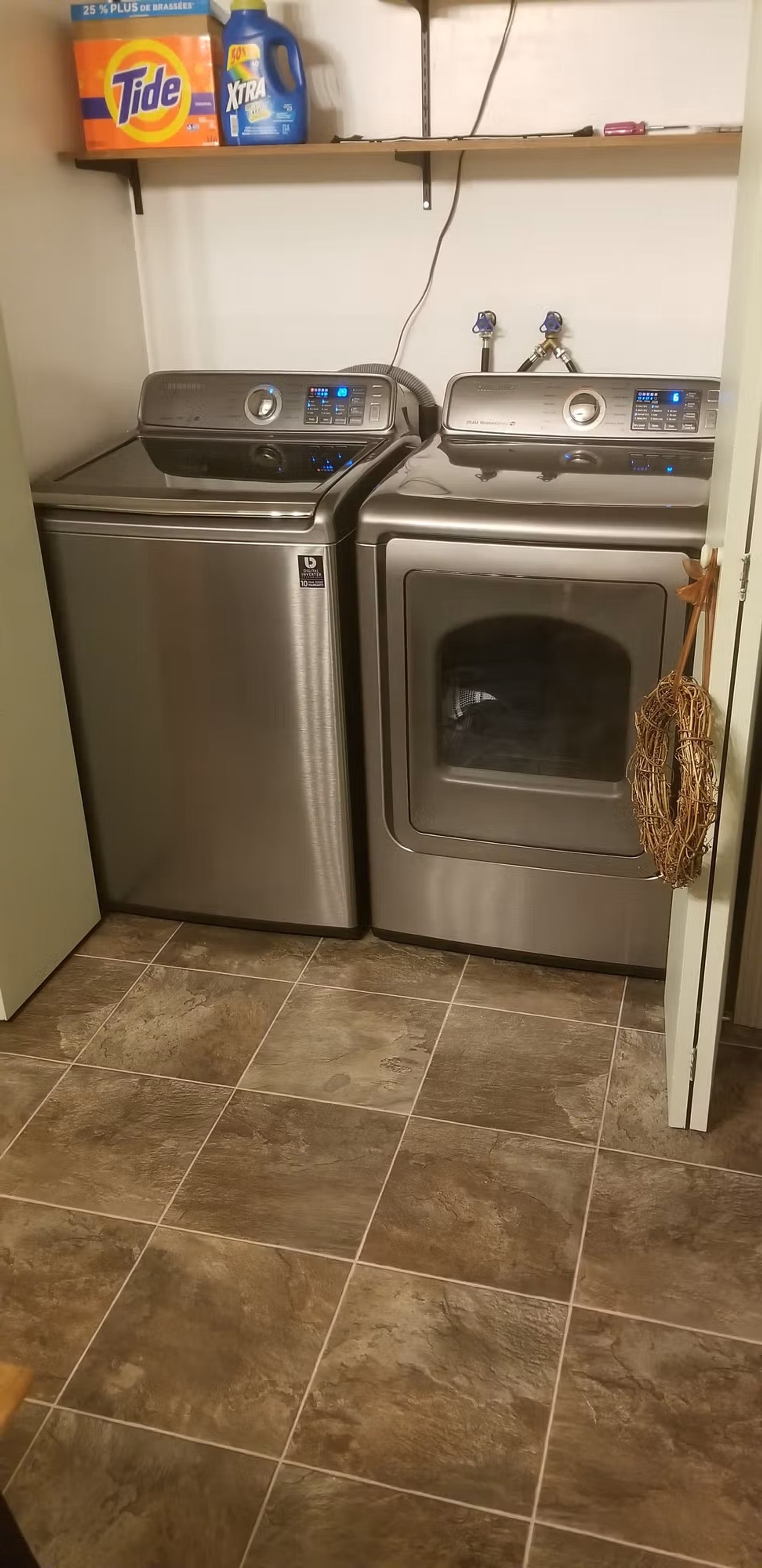 Laundry room with stainless steel washer and dryer, shelves, and tiled floor.