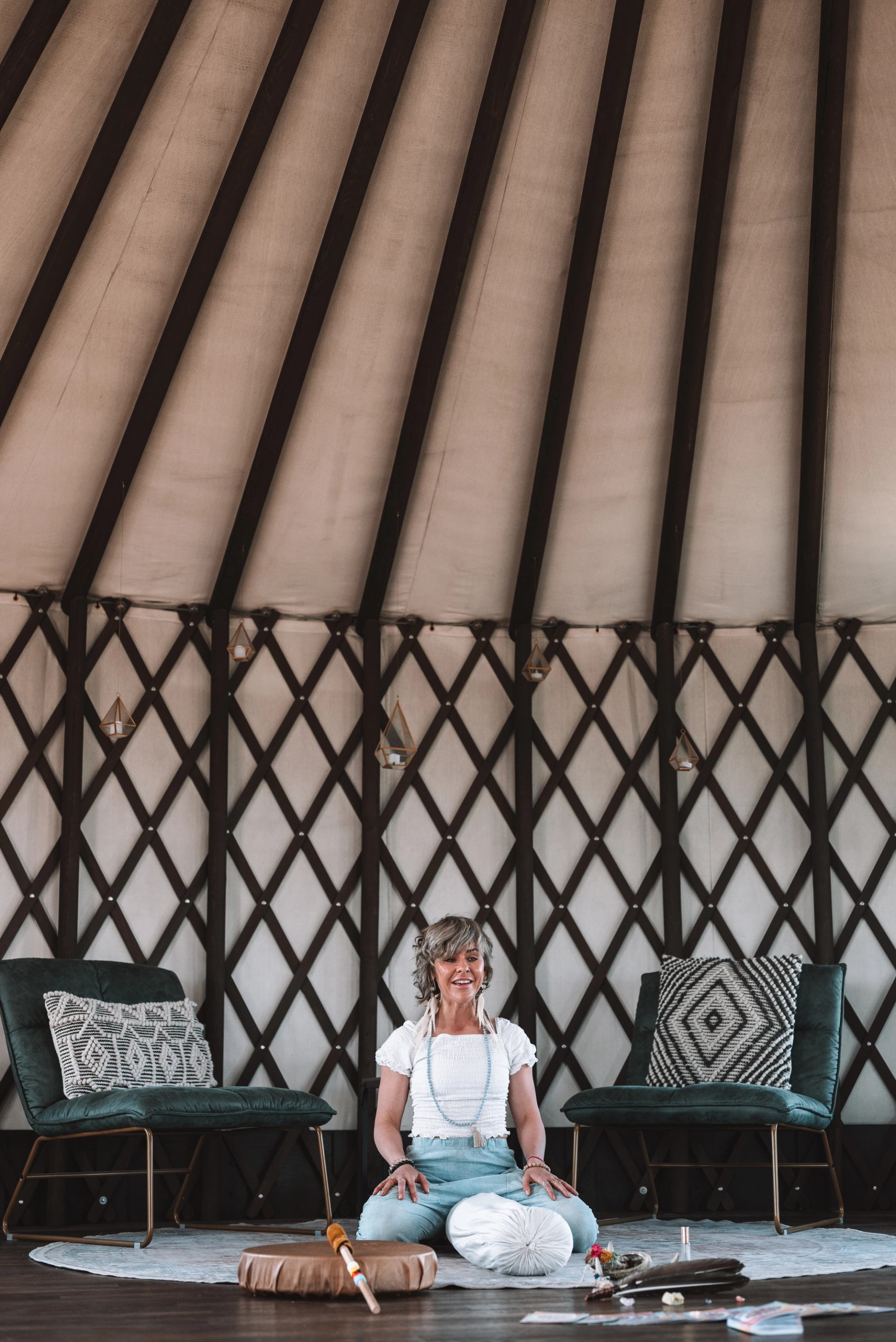 Person kneels on a rug between green chairs inside a lattice-framed yurt.