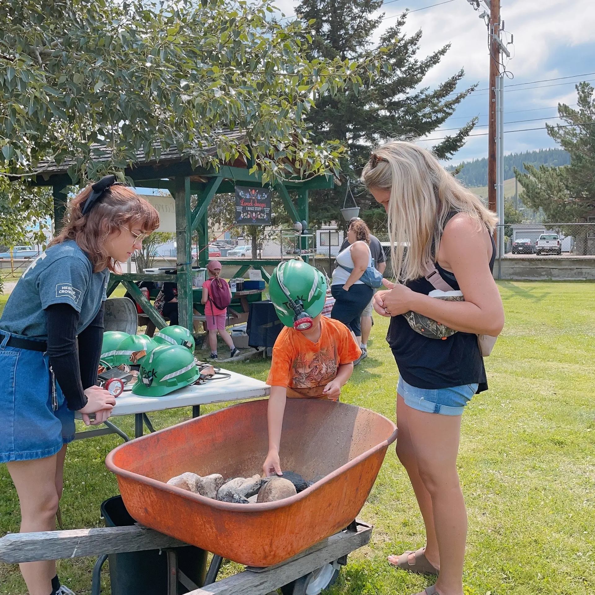Festival volunteers guide children around a fire bowl and painted green helmets on a table.