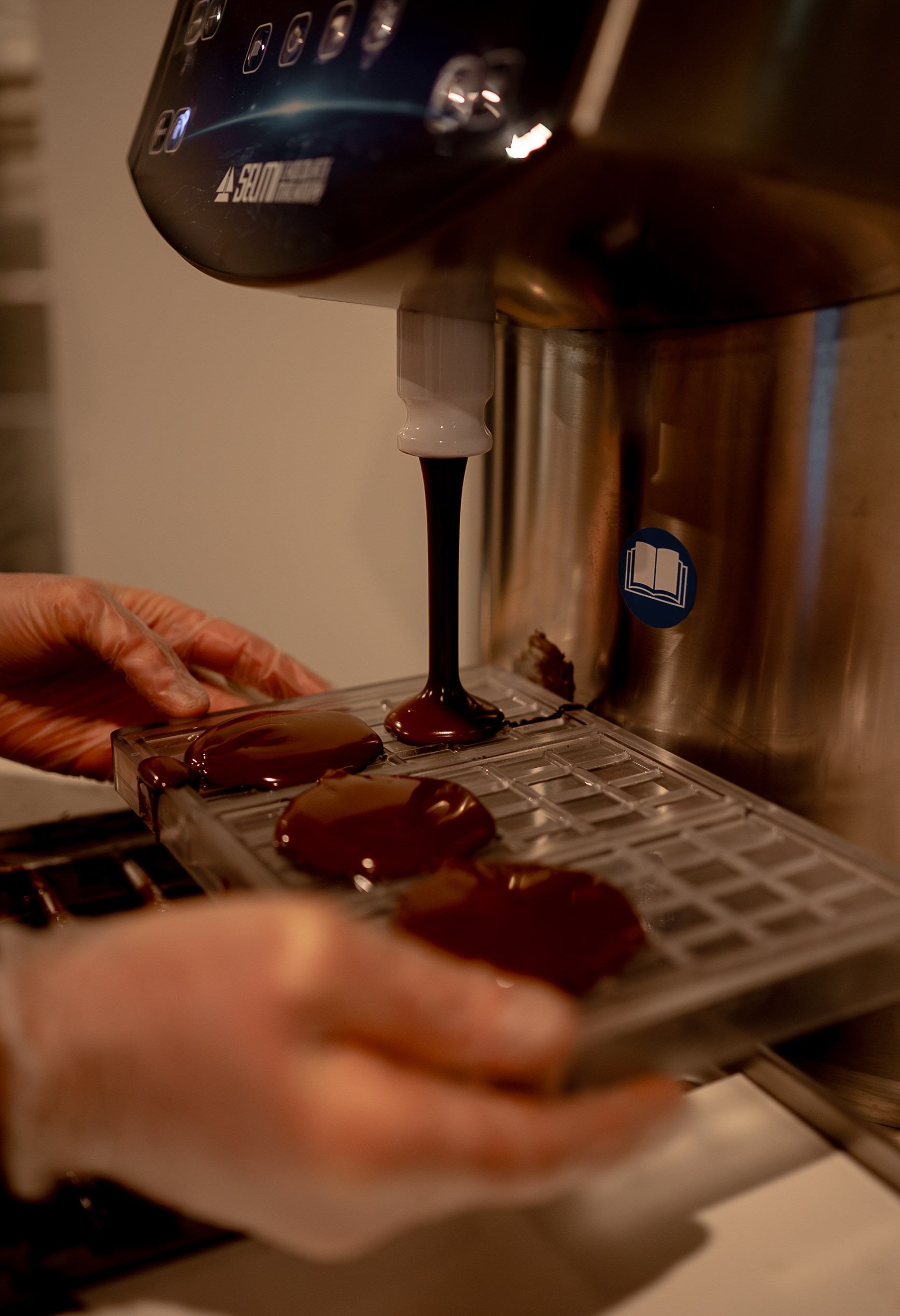 Chocolate machine dispensing dark chocolate onto a metal cooling tray.