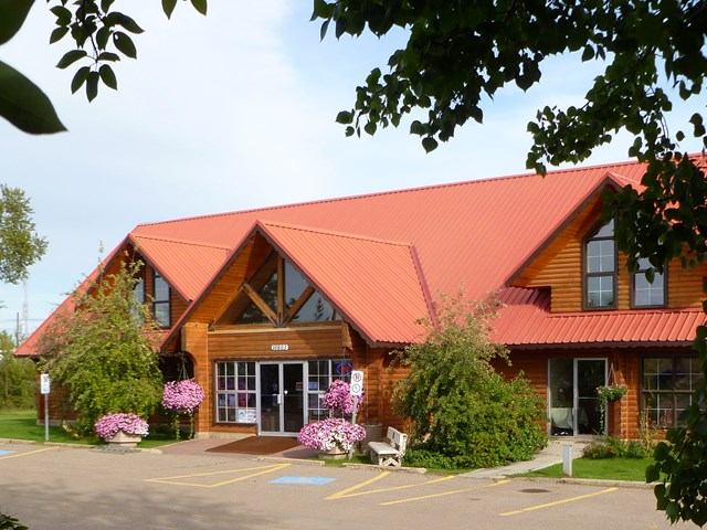 Wooden building with red roof, large windows, and colorful flowers out front.