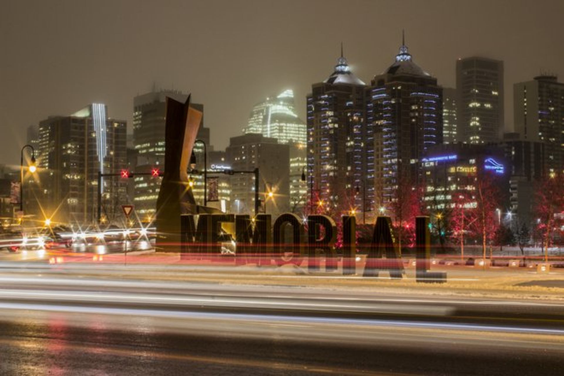 The Memorial sculpture at Poppy Plaza is framed by city lights and passing traffic at night.