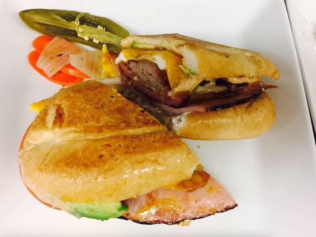 Two sandwiches on a white plate with pickles and sliced vegetables, restaurant meal.