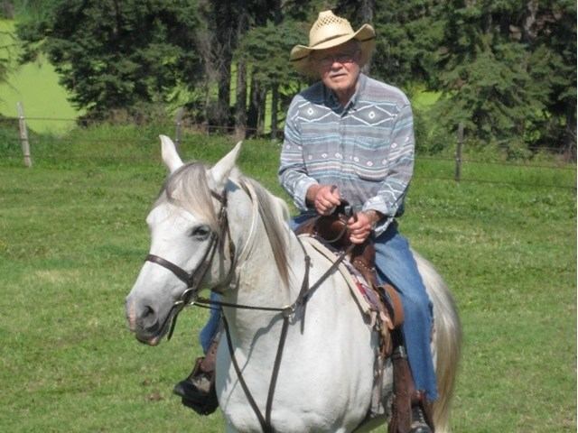 Rider on a white horse trotting through a green field at Keno Hills Stable.