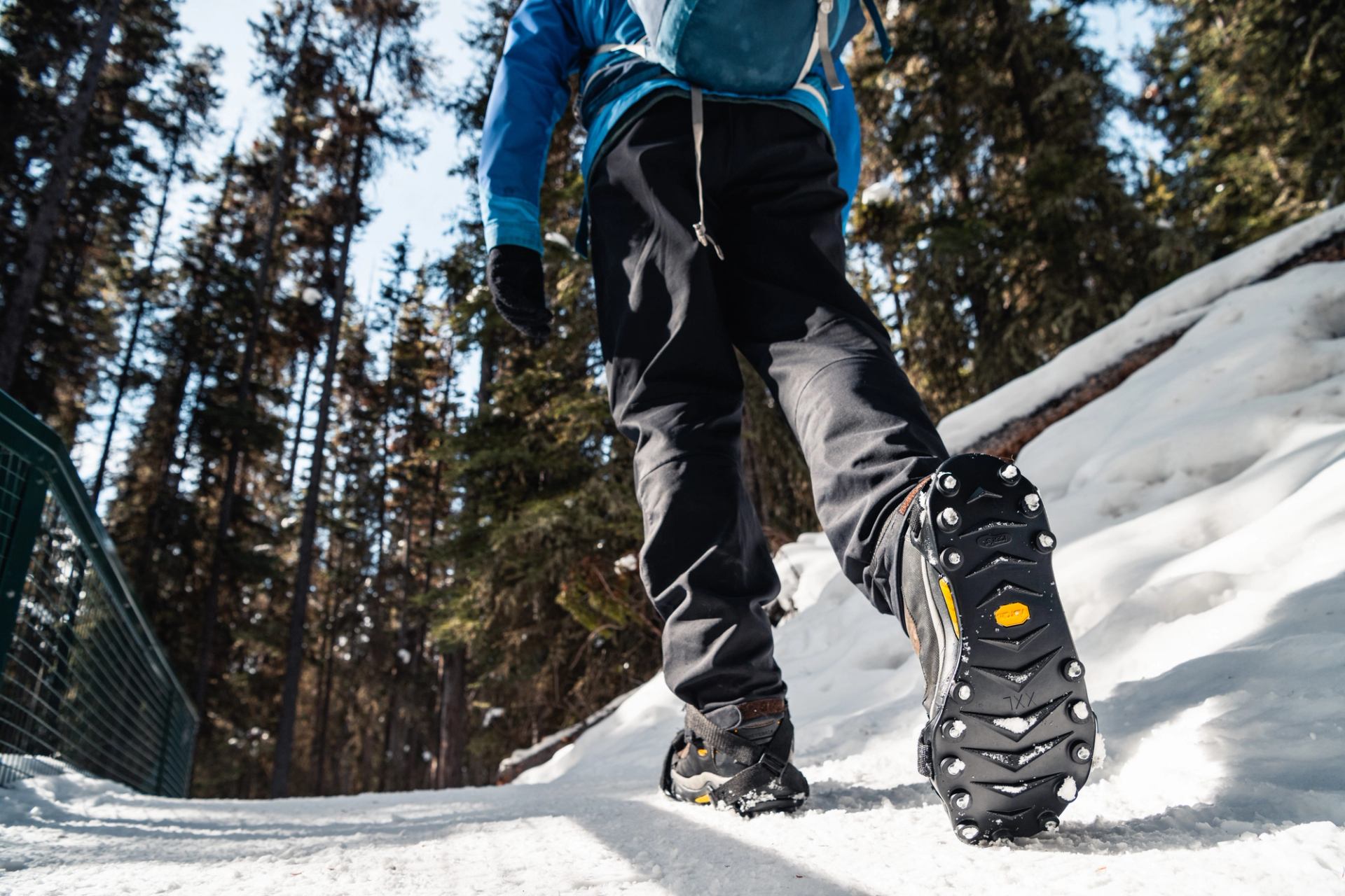 Close‑up of a hiker’s boots with ice cleats walking on a snowy forest trail in Banff.