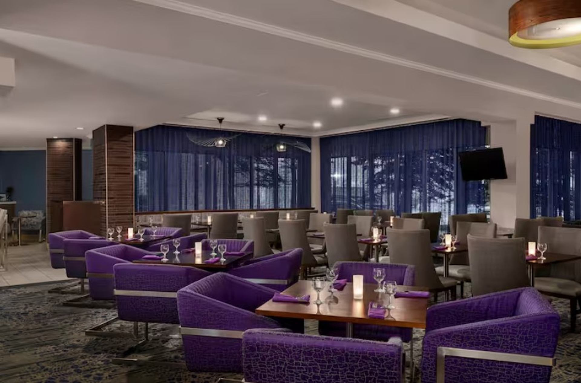 Stylish hotel restaurant with purple lounge chairs and neatly set dining tables.