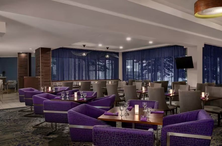 Stylish hotel restaurant with purple lounge chairs and neatly set dining tables.