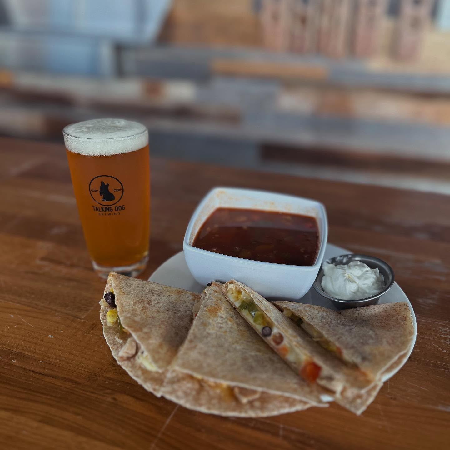 Pint of beer served with quesadilla slices, soup bowl, and sour cream