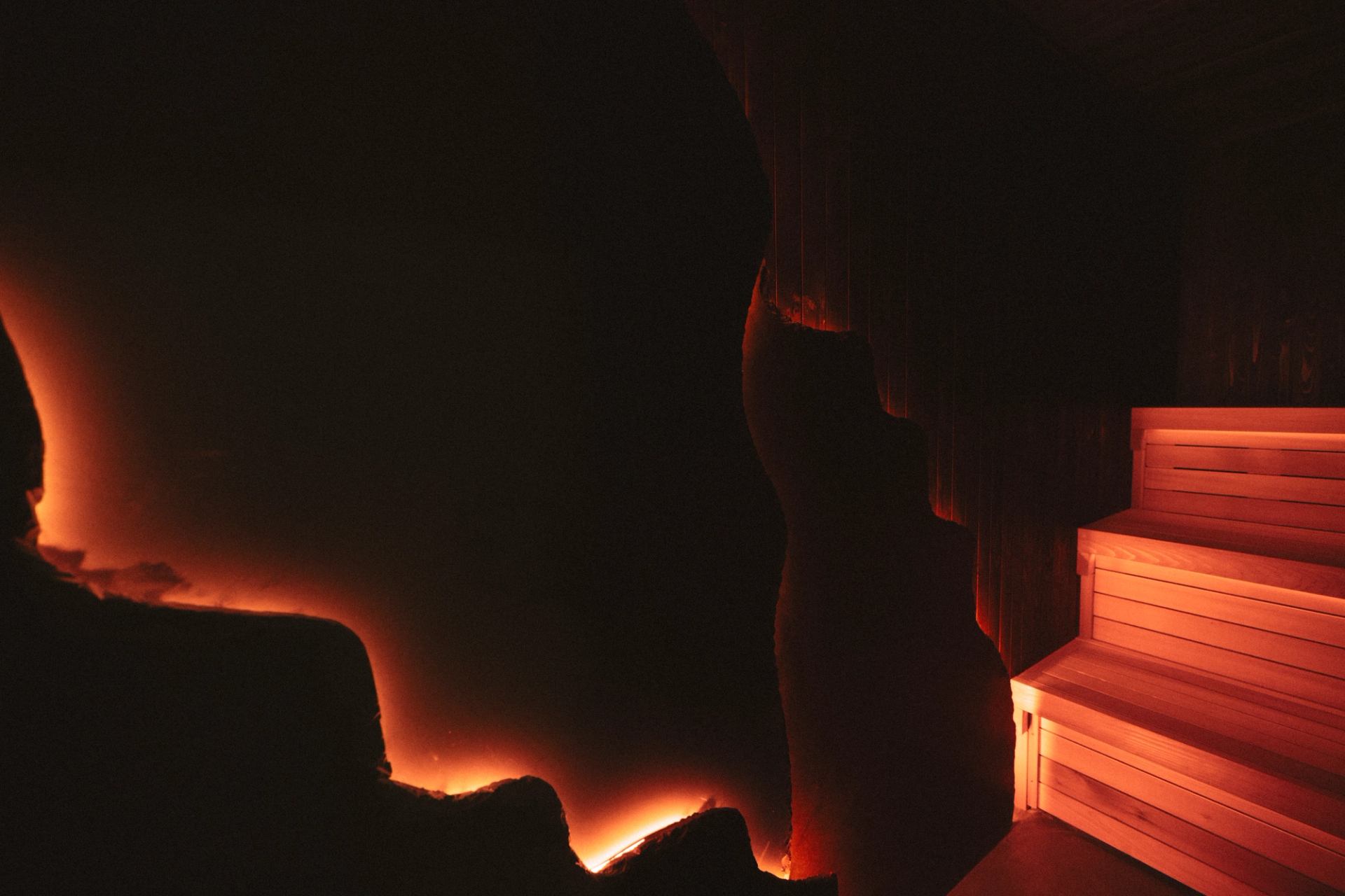 Dimly lit sauna interior with glowing rock formations and wooden bench steps.