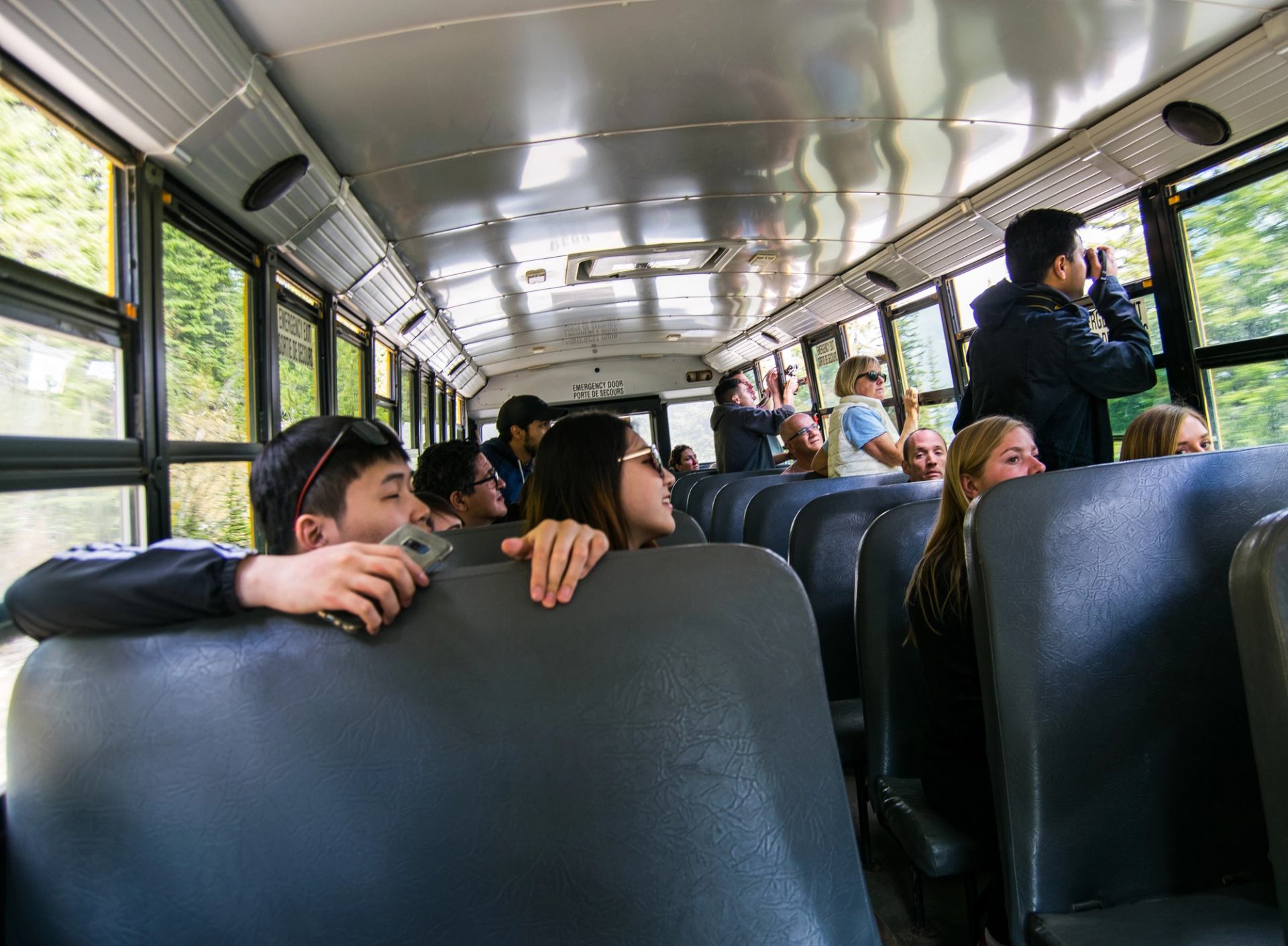 People looking out bus windows, some with binoculars, on a scenic trip.