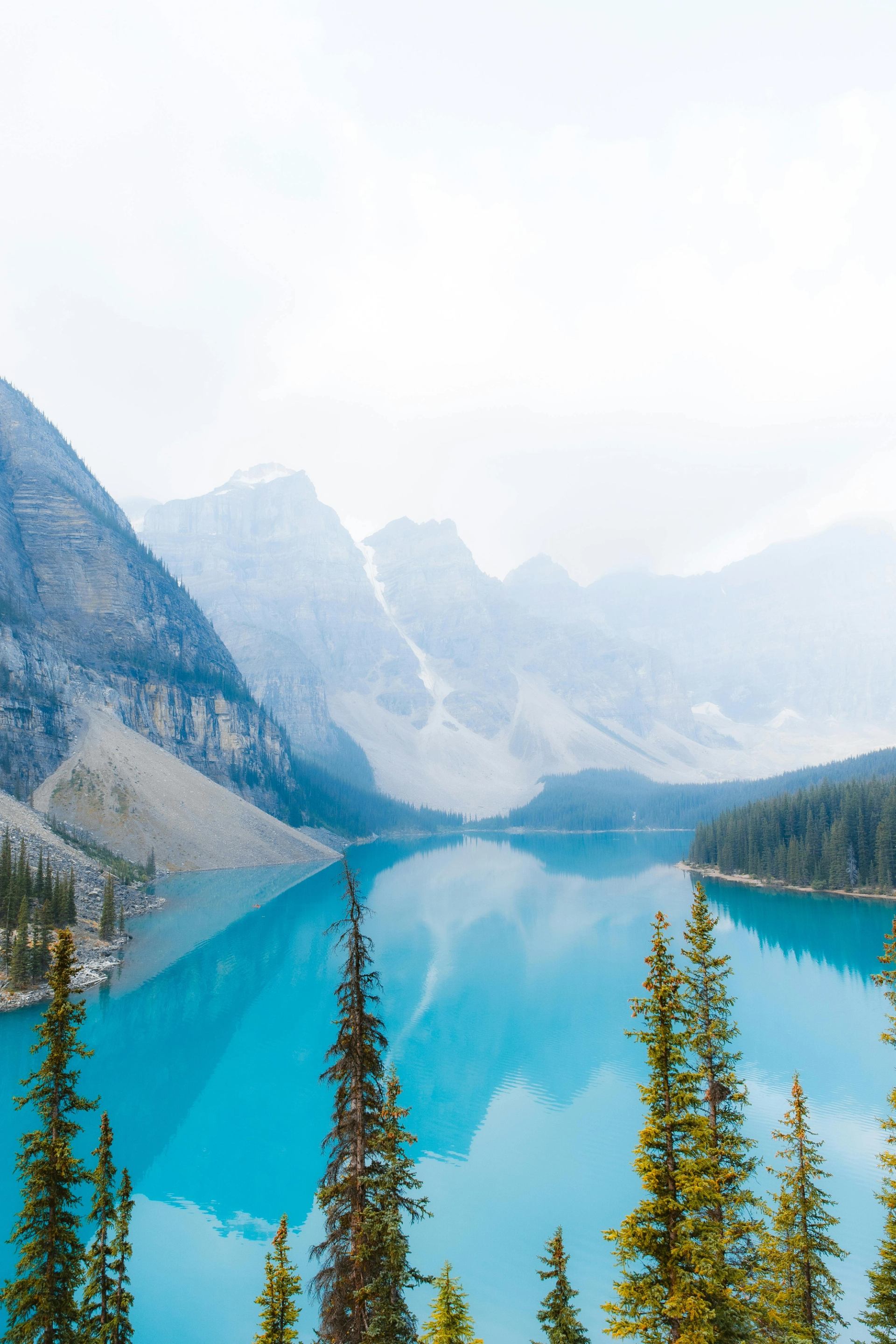 A vibrant turquoise lake reflecting misty mountains and evergreen trees.