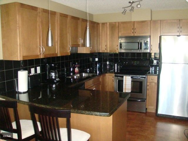 Modern kitchen with stainless steel appliances, black tile backsplash, and wood cabinets.