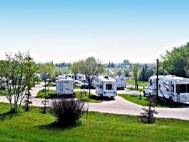 RV park with white recreational vehicles, green landscape, and blue sky.
