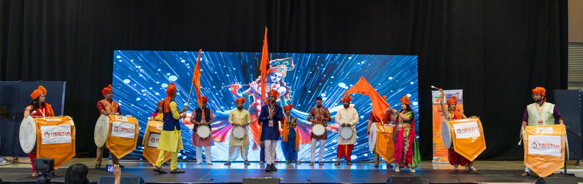 Performers in colourful traditional clothing play drums and wave flags onstage.