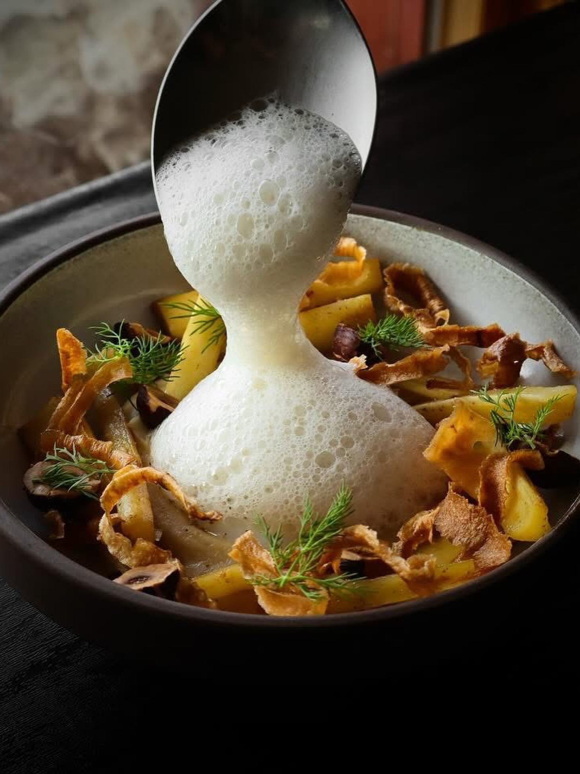 Foam poured from spoon over plated potatoes, mushrooms, fried strips and fresh dill.