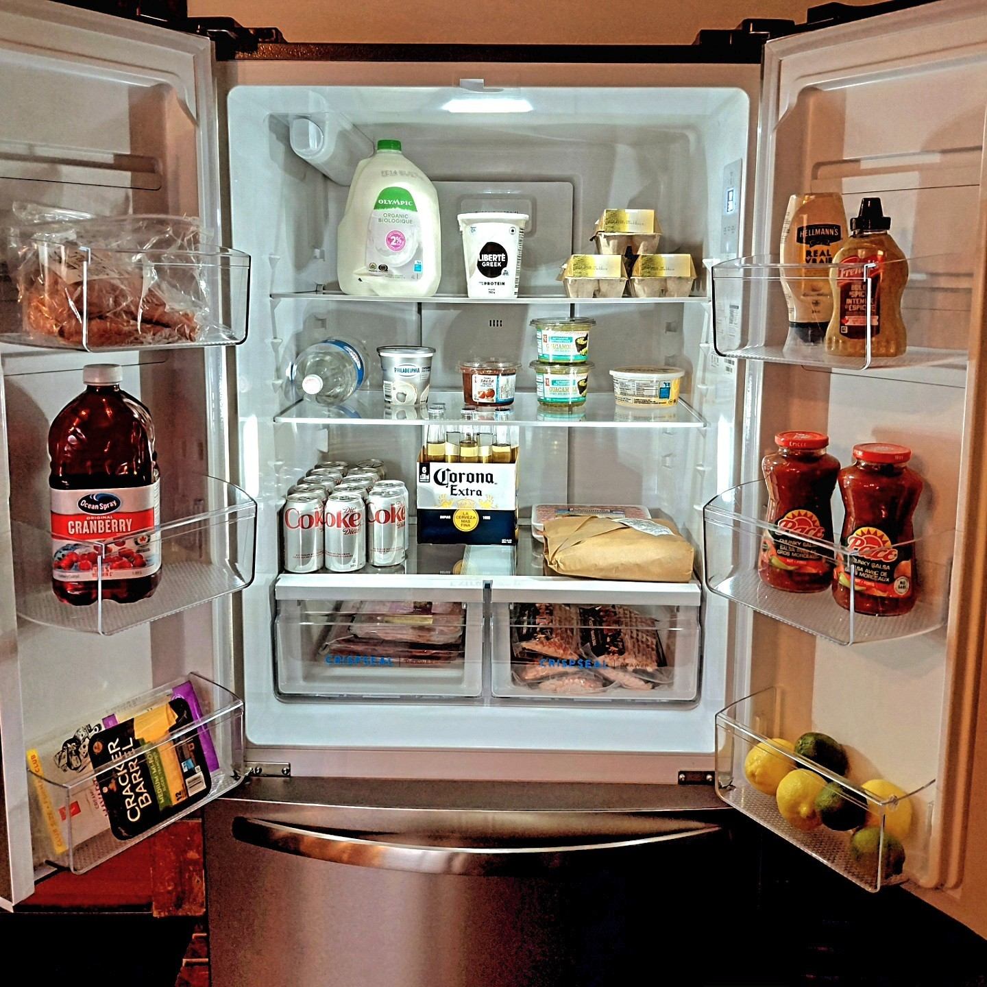 Open refrigerator stocked with dairy, eggs, drinks, condiments, meat and citrus fruit.
