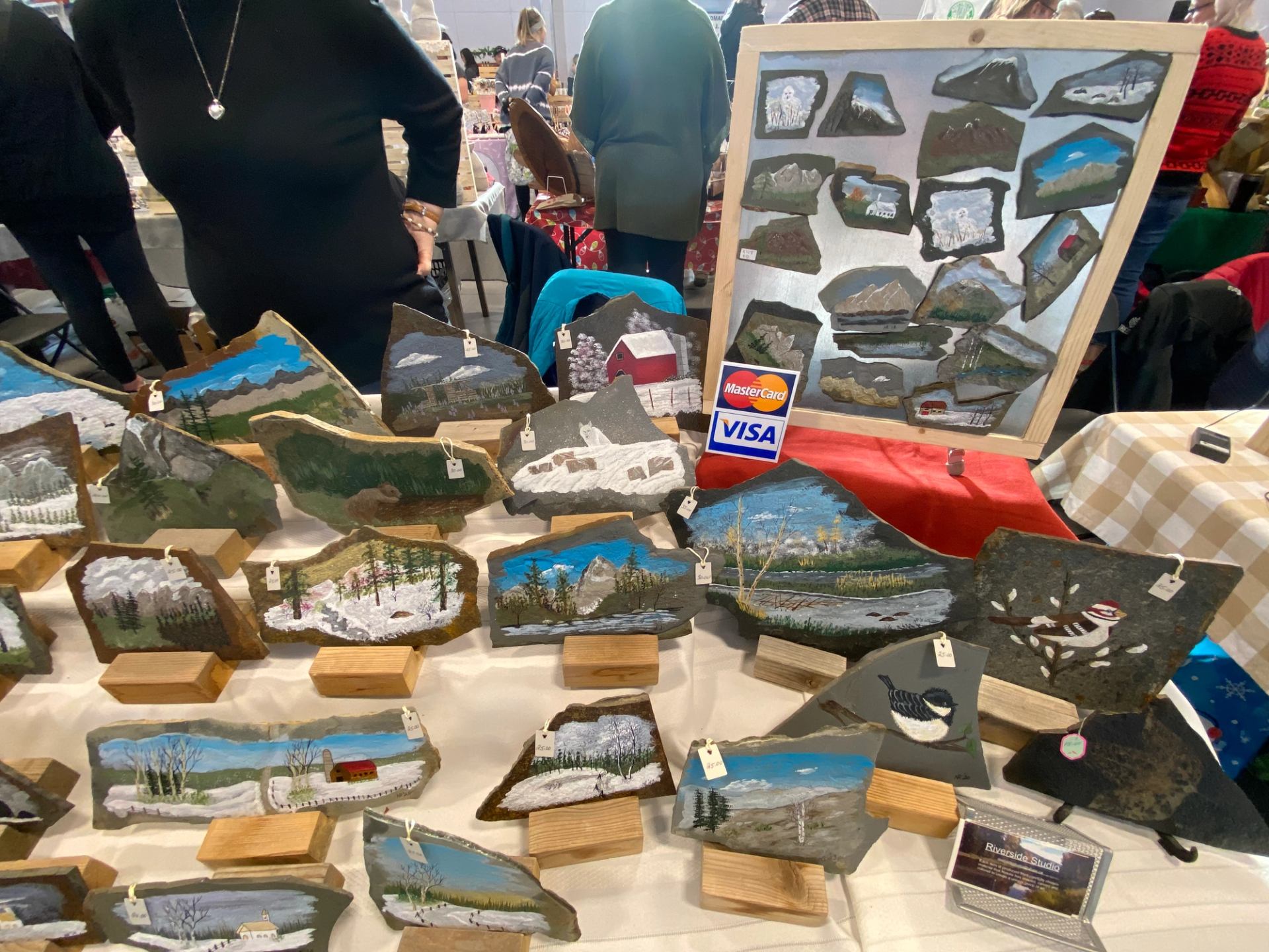 Painted rock art featuring scenic landscapes displayed on a holiday market table.