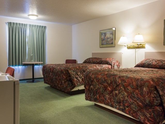 Hotel room with four beds, lamps, curtains, and a small table near the window.